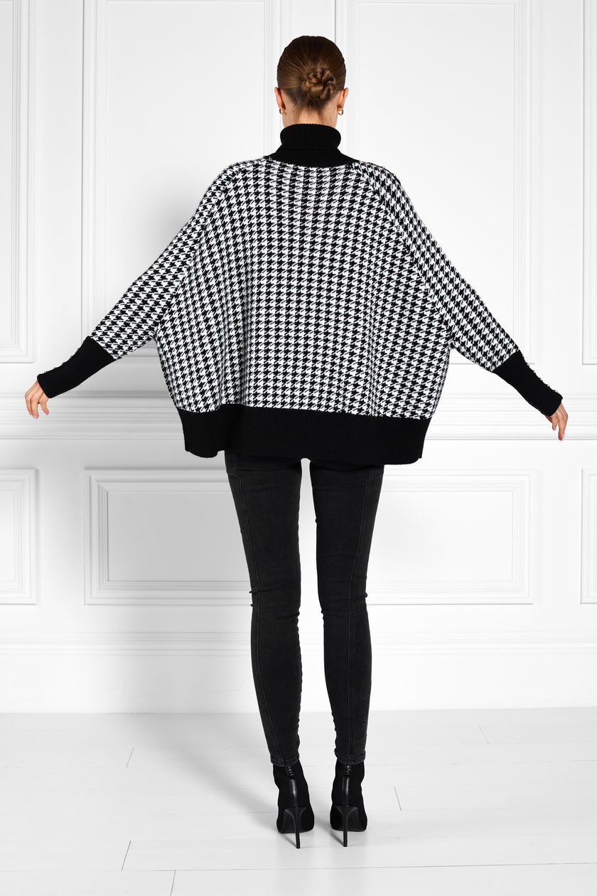 back of womens funnel neck batwing shaped cape in a white and black houndstooth knit with split side detail and contrast black neckline cuffs and hem