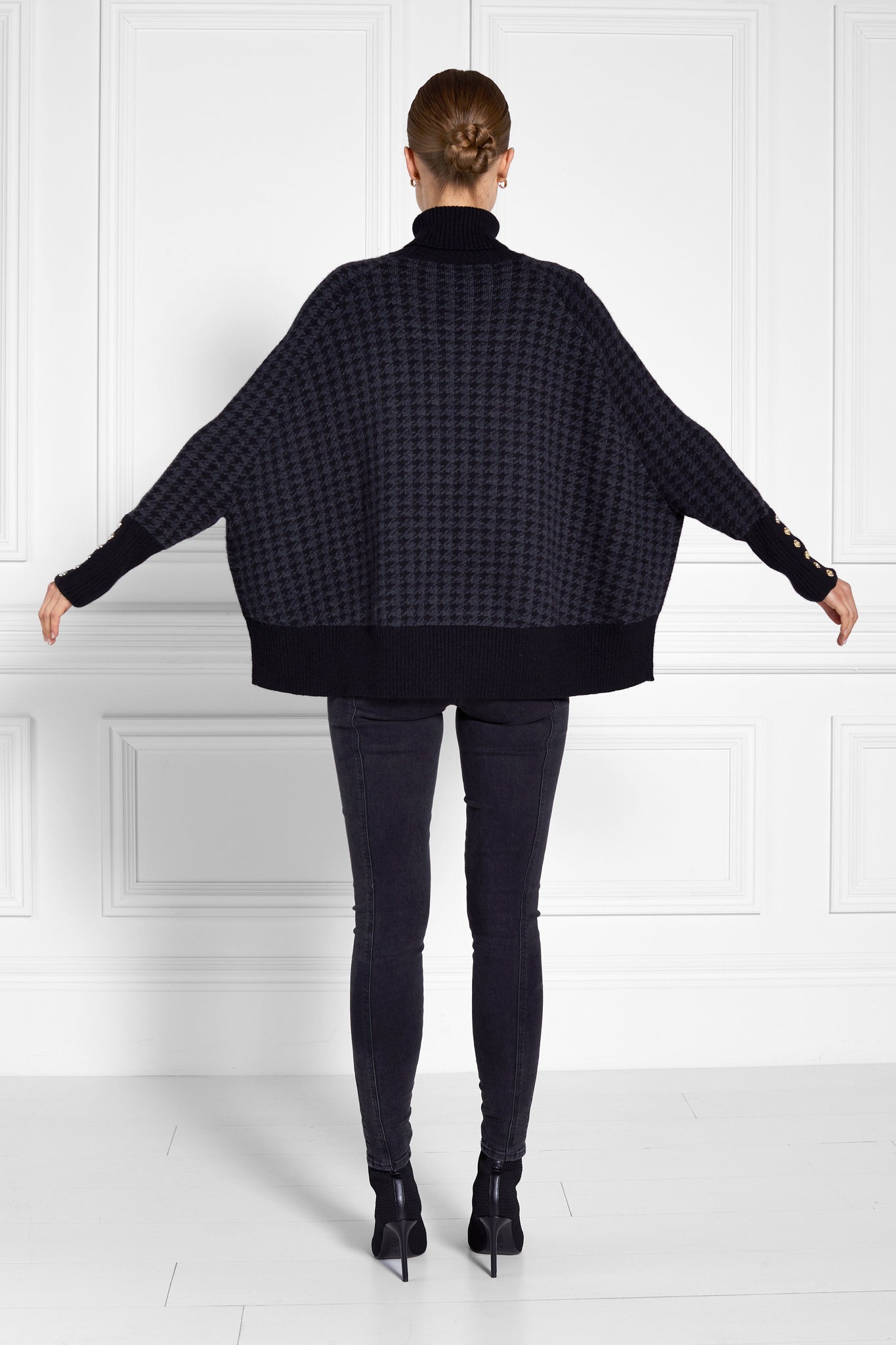 back of womens funnel neck batwing shaped cape in a grey and black houndstooth knit with split side detail and contrast black neckline cuffs and hem