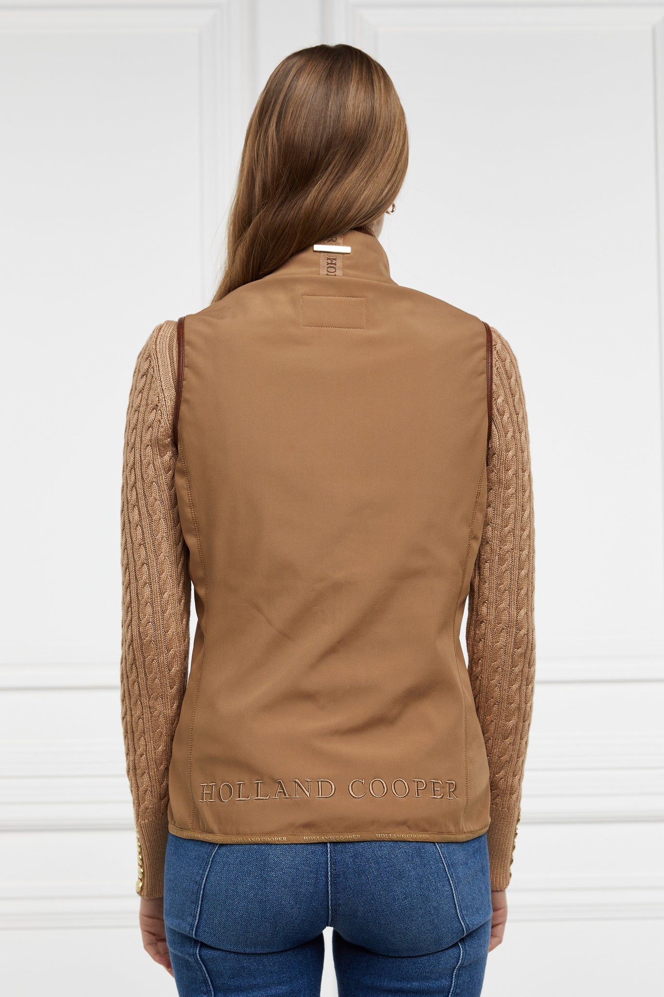 back of womens light brown gilet with dark brown leather seams with a logo along the bottom and on the collar