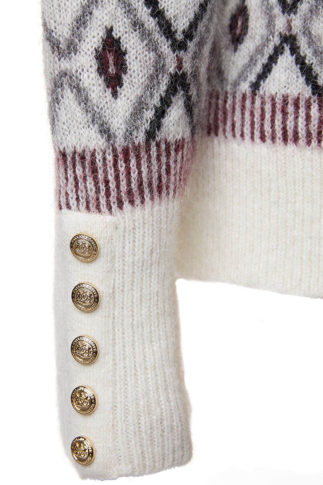 gold button detail on cuffs of a classic cream roll neck jumper with fairisle knit in red and grey around the shoulders waistline and cuffs and a split ribbed hem 