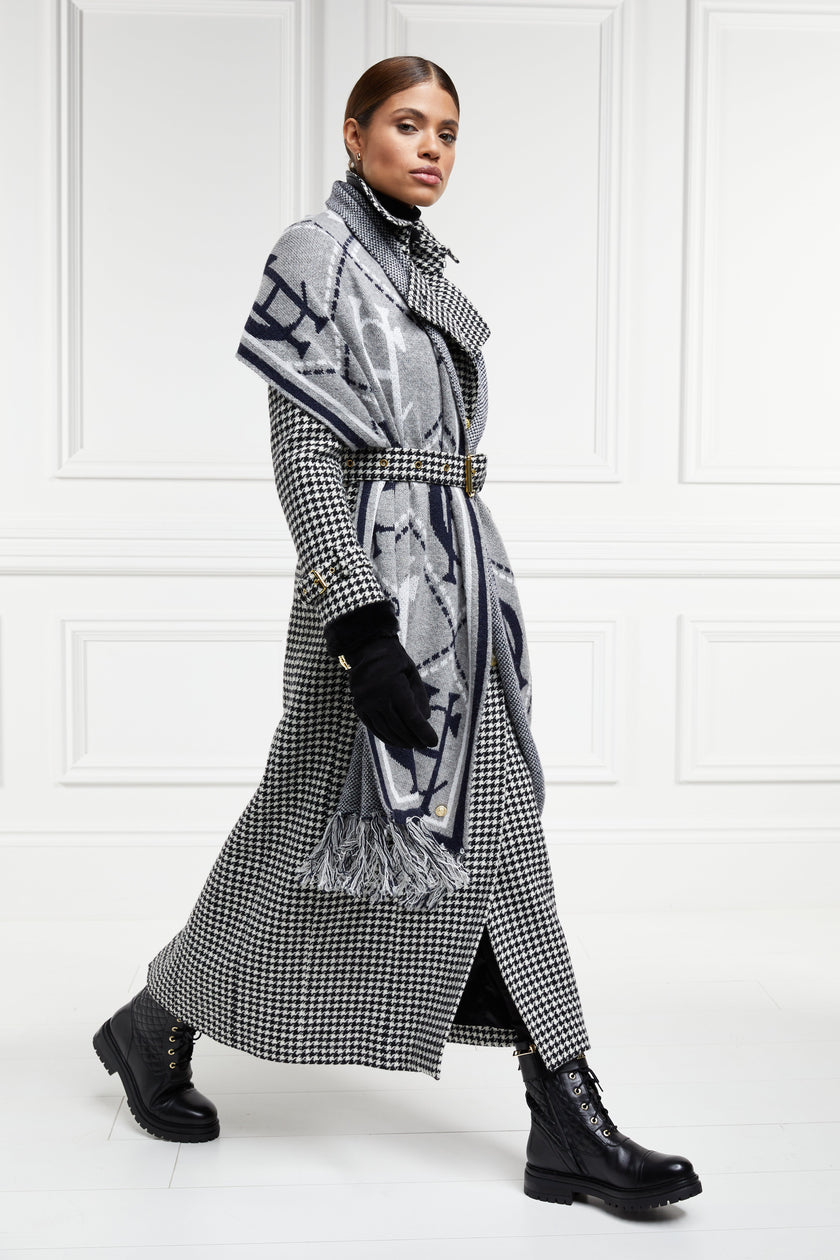 walking in womens black and white houndstooth double breasted full length wool trench coat with grey and navy HC logo print scarf and womens suede black gloves