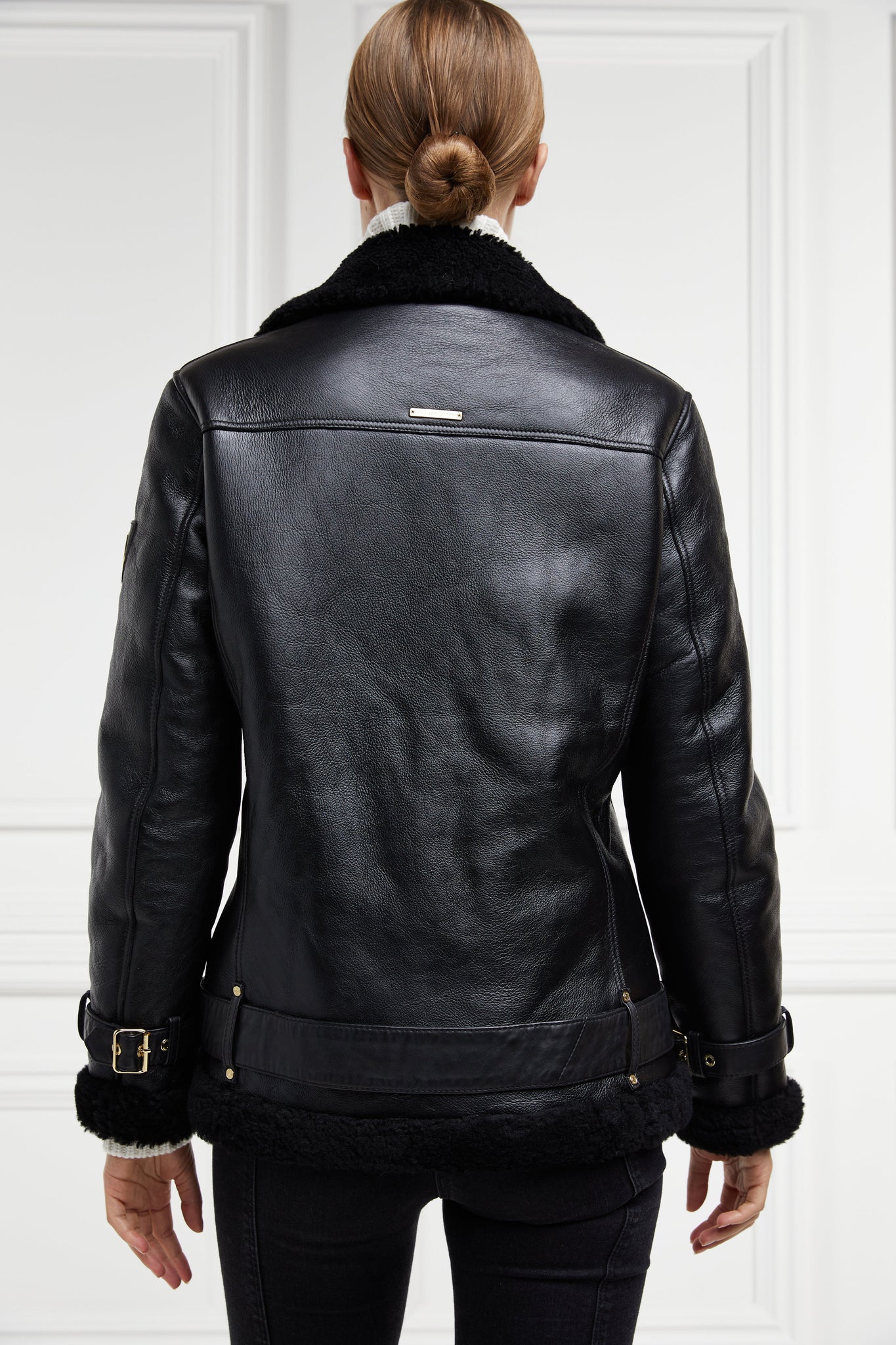 back of classic aviator jacket in black leather with back shearling inside that accents the cuffs hem and collar with belt detail on the hem and cuffs three pockets and angular zip fastening