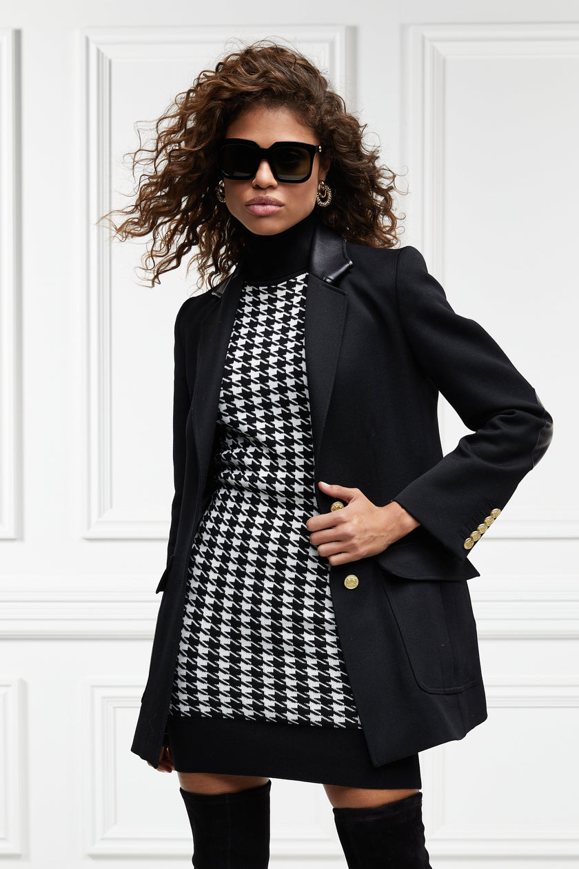 womens black and white houndstooth sleeveless mini dress with black contrast arm holes roll neck and hem with gold button details on shoulders under black double breasted blazer