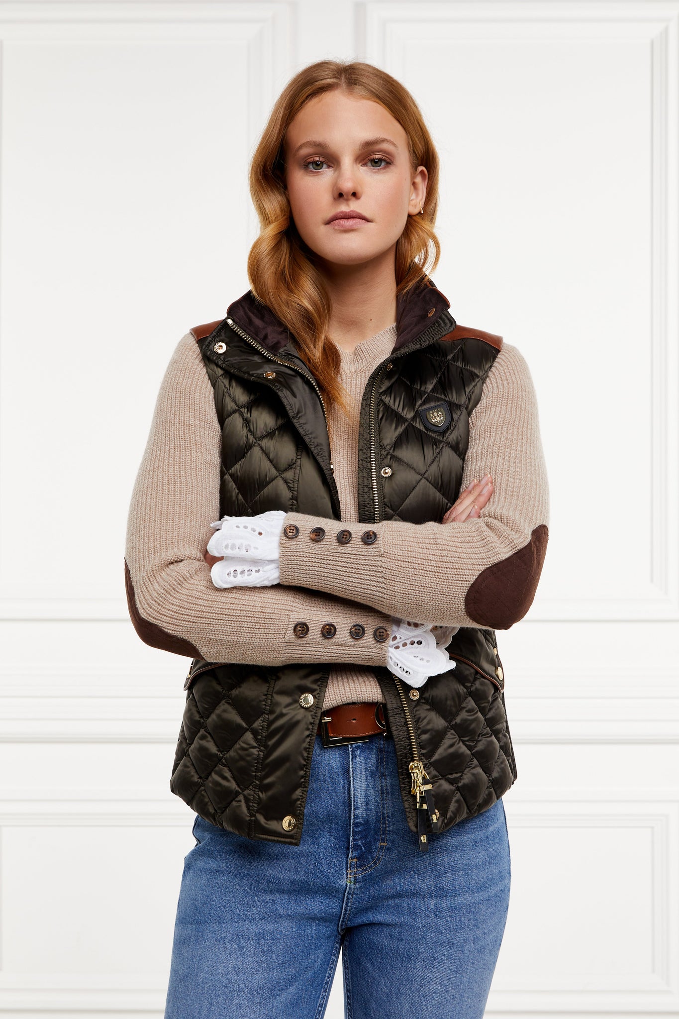 classic crew neck slim fit merino wool jumper in taupe with brown faux suede gunpatch on shoulder and quilted elbow patches in the same brown suede material worn under a diamond quilted gilet in khaki