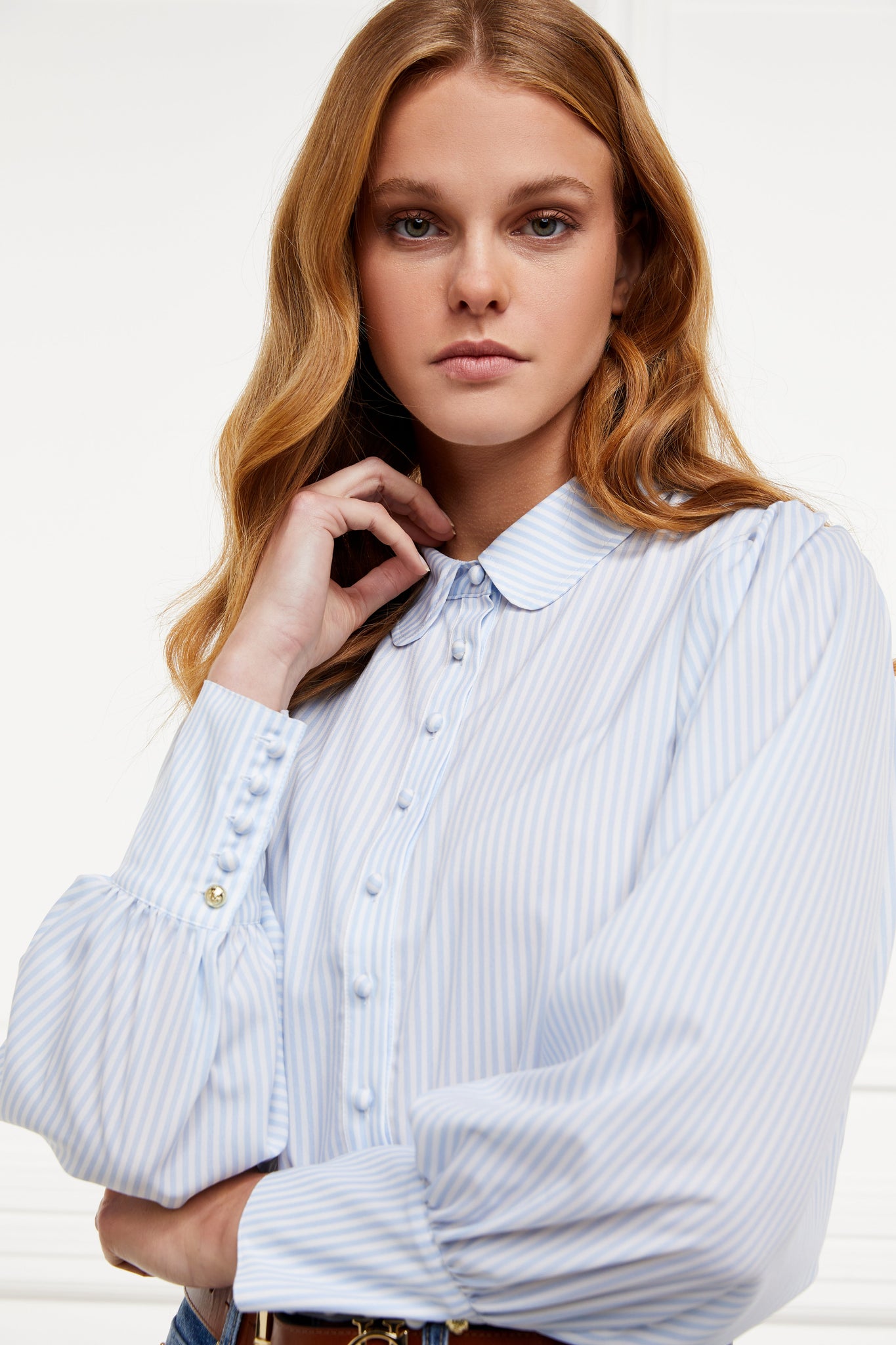 A classic fitted shirt with long sleeves and subtle puffy shoulders with thin blue and white stipe print design with extra long cuffs and rounded collar detailed with fabric buttons 