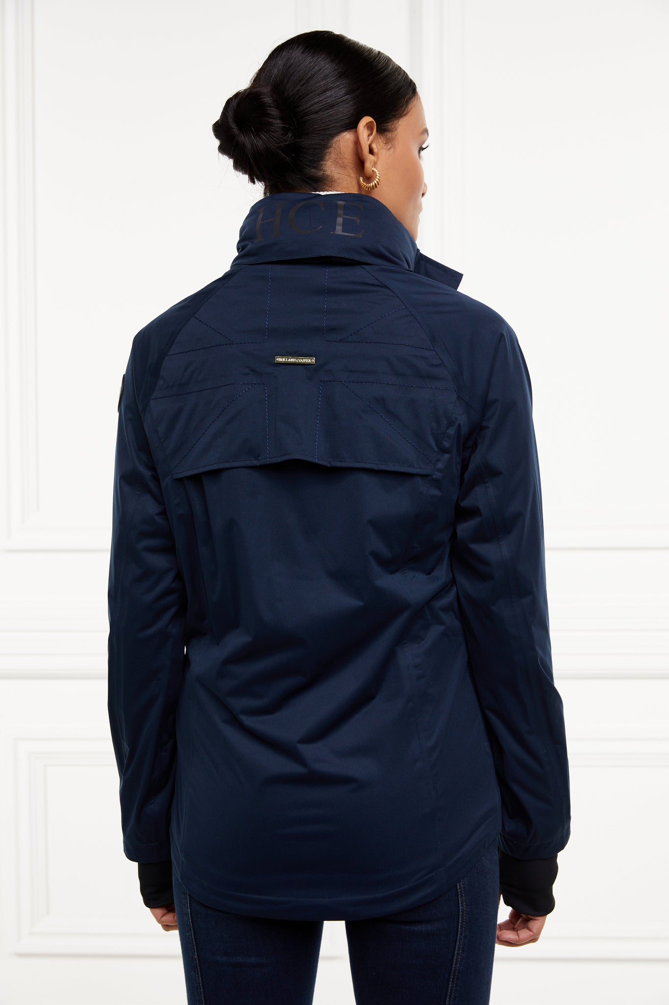 Back of Womens waterproof navy jacket with stowaway hood storm cuffs and two pockets at hip with waterproof zip fastening showing back vent at top of back