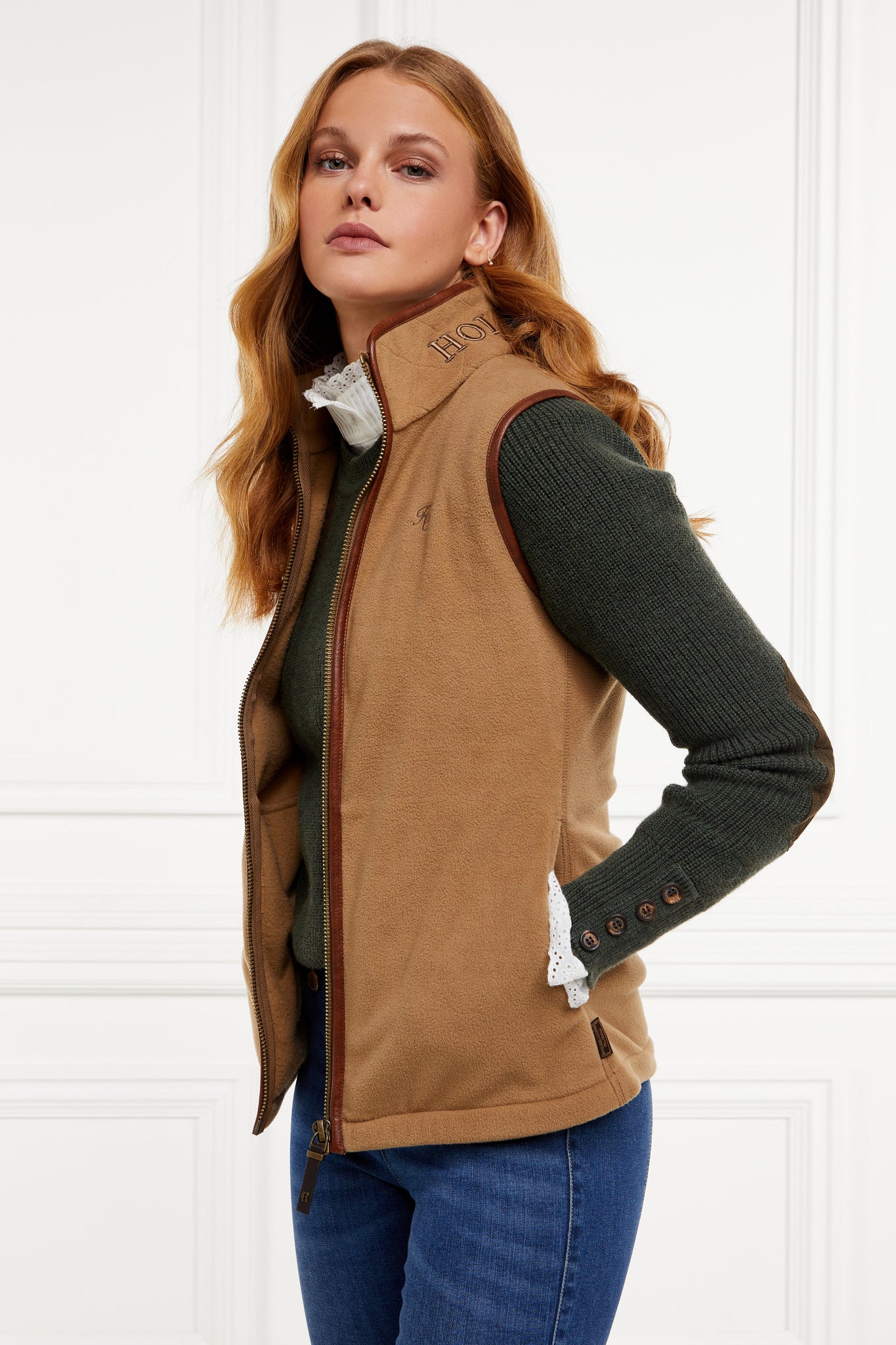 womens fleece gilet in light brown with dark brown leather piping around armholes neckline and down the front zip fastening a dark green knitted sweatshirt a white long sleeve shirt and dark denim skinny jeans