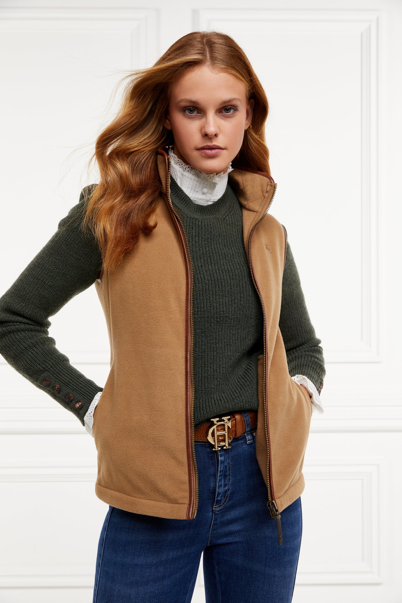 womens fleece gilet in light brown with dark brown leather piping around armholes neckline and down the front zip fastening a dark green knitted sweatshirt a white long sleeve shirt and dark denim skinny jeans