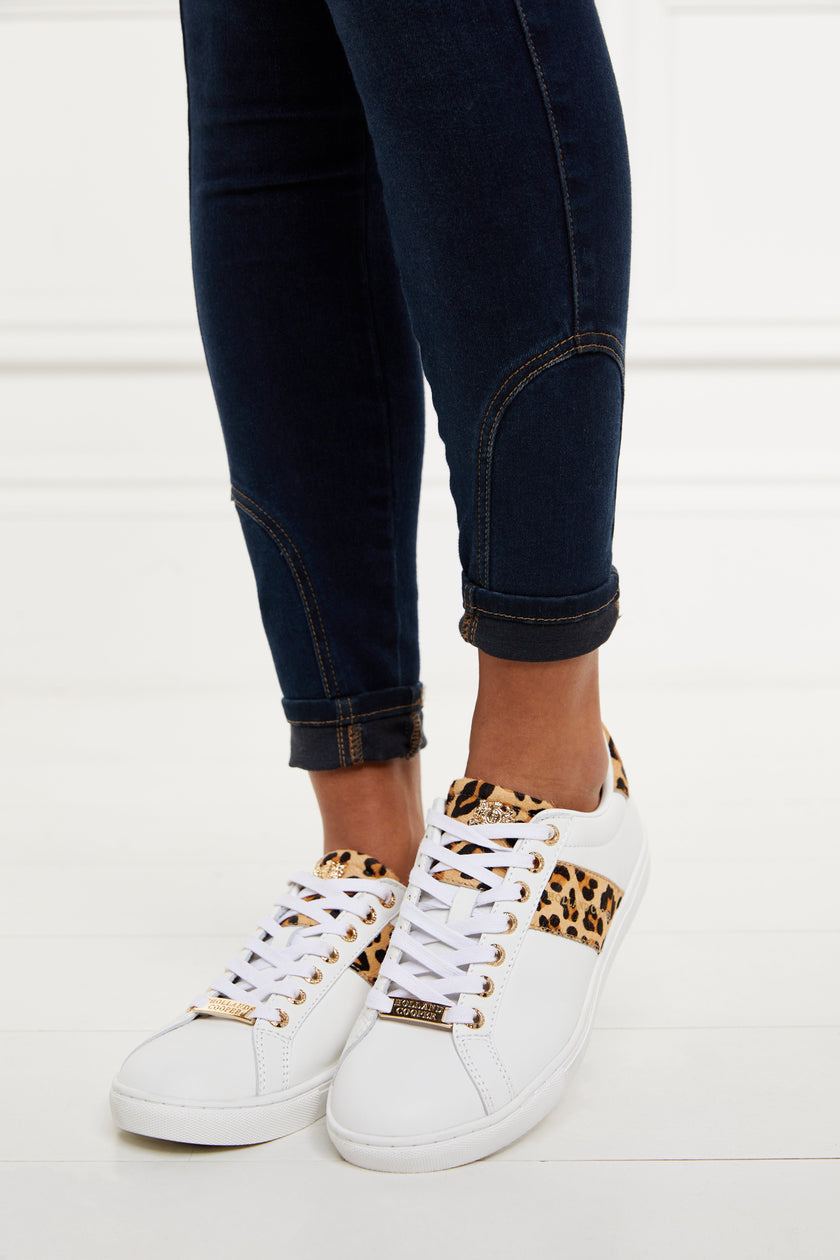 white leather trainers with white laces detailed with a diagonal stripe of leopard print on the side with gold foil branding and a leopard print heel and tongue with gold hardware. Worn with rolled up denim skinny jeans.