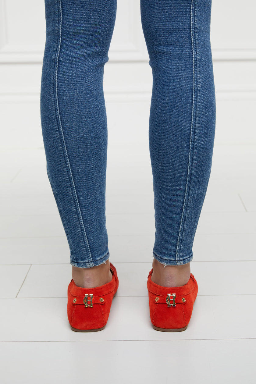 back of orange suede loafers with a leather sole and gold hardware paired with denim jeans