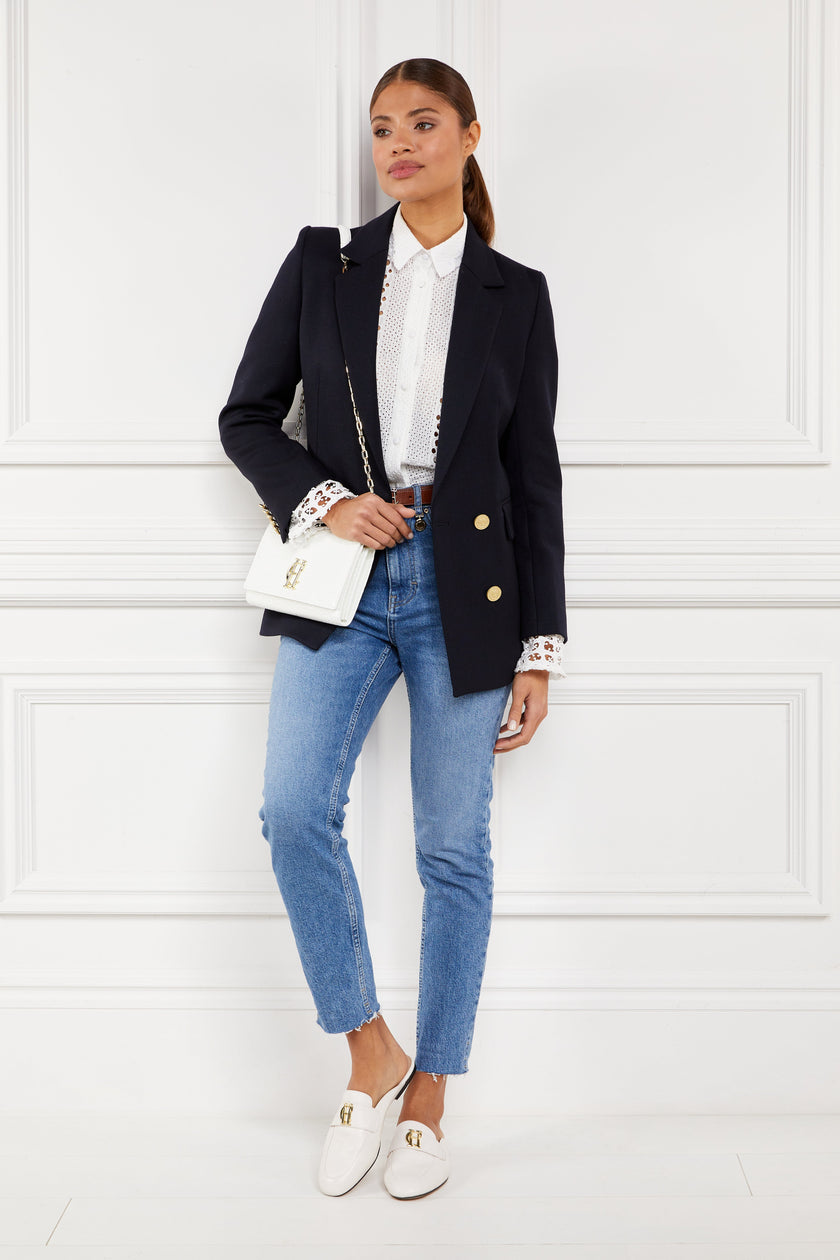 white leather backless loafers with a slightly pointed toe and gold hardware to the top worn with slim denim jeans, white broderie lace shits under a navy blazer with a white croc embossed leather clutch bag and gold chain strap