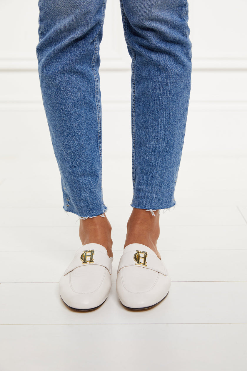 white leather backless loafers with a slightly pointed toe and gold hardware to the top worn with slim denim jeans with a frayed edge