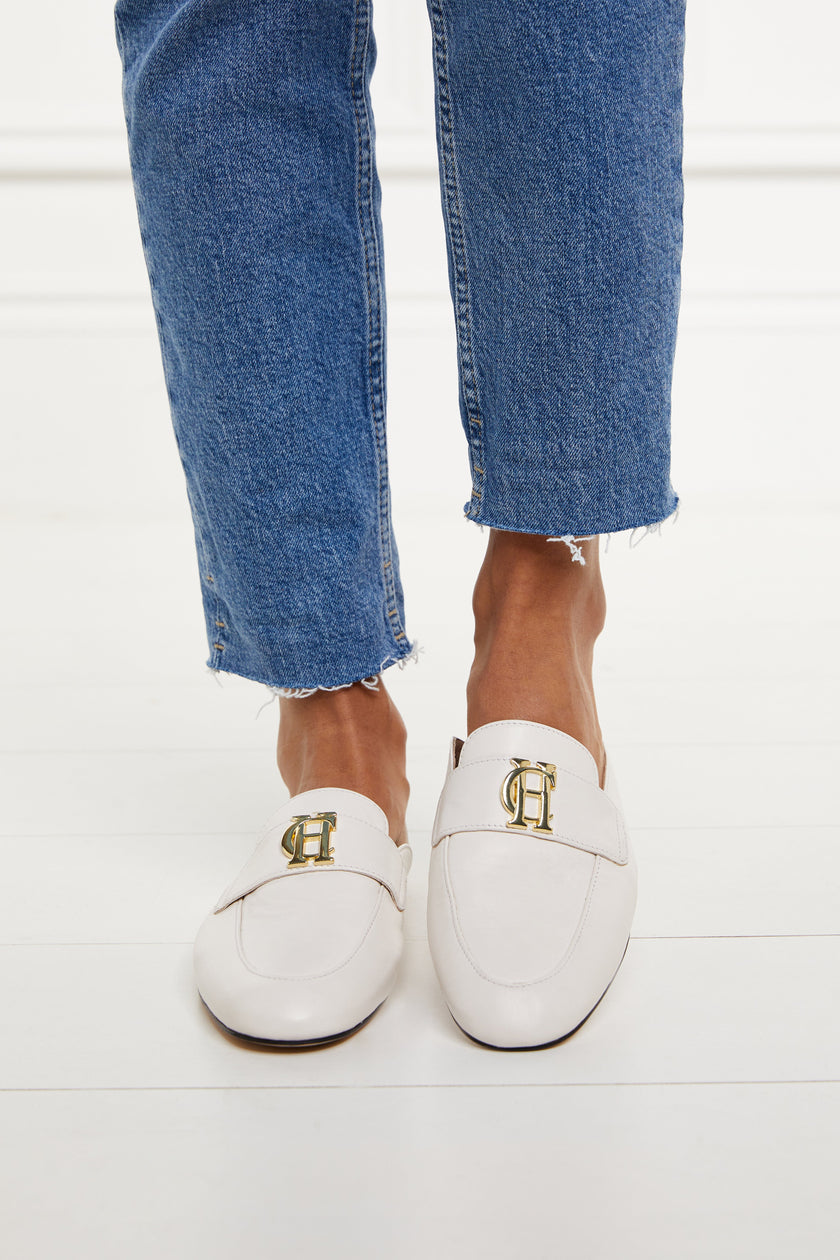 white leather backless loafers with a slightly pointed toe and gold hardware to the top worn with slim denim jeans with a frayed edge