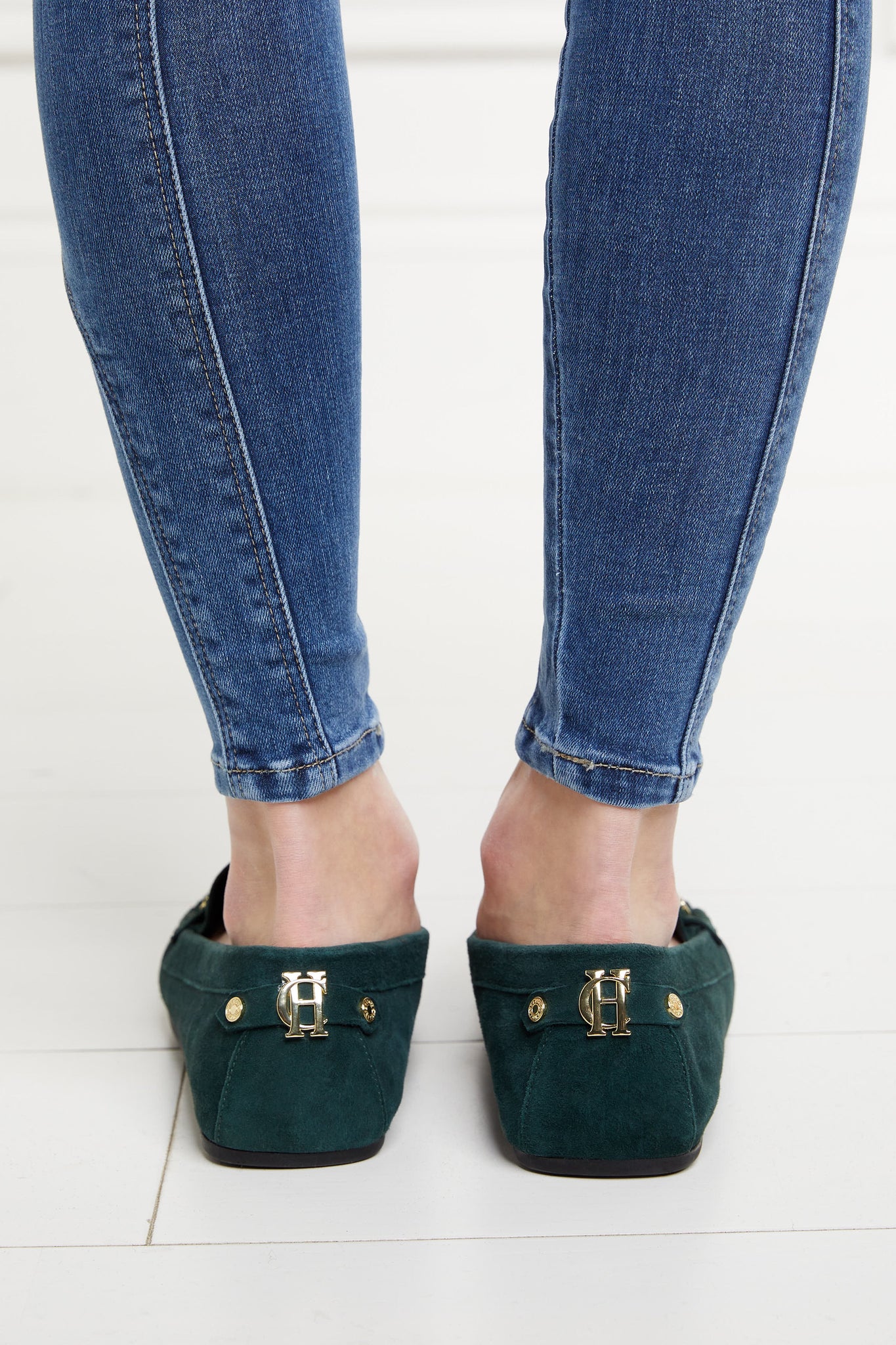 Back of classic emerald green suede loafers with a leather sole and gold hardware paired with a classic denim skinny jean