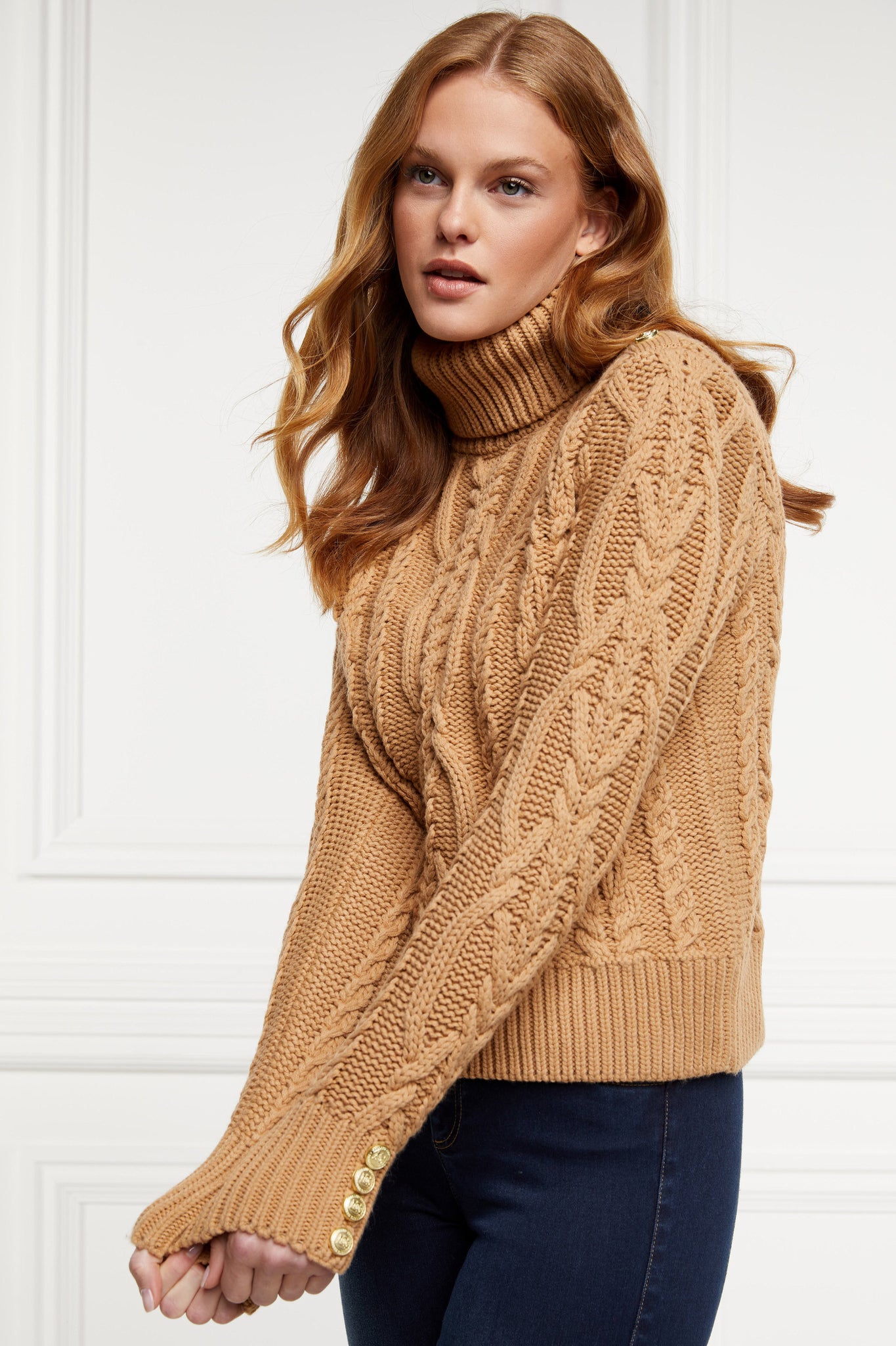 a chunky cable knit roll neck jumper in camel with dropped shoulders and thick ribbed cable trims and gold buttons on cuffs and collar