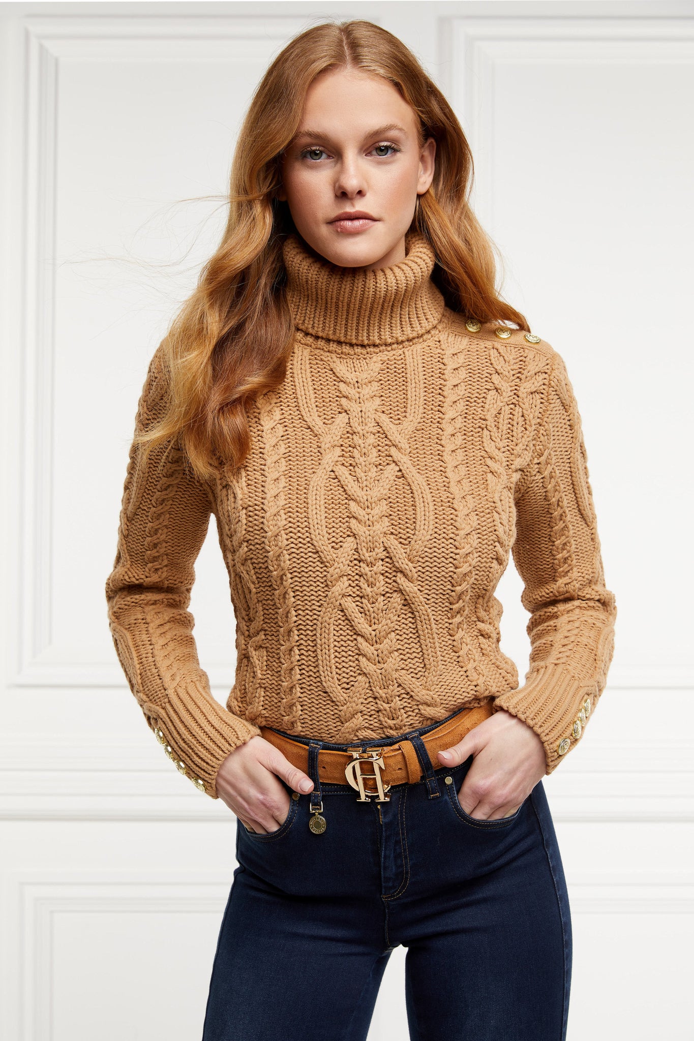 a chunky cable knit roll neck jumper in camel with dropped shoulders and thick ribbed cable trims and gold buttons on cuffs and collar