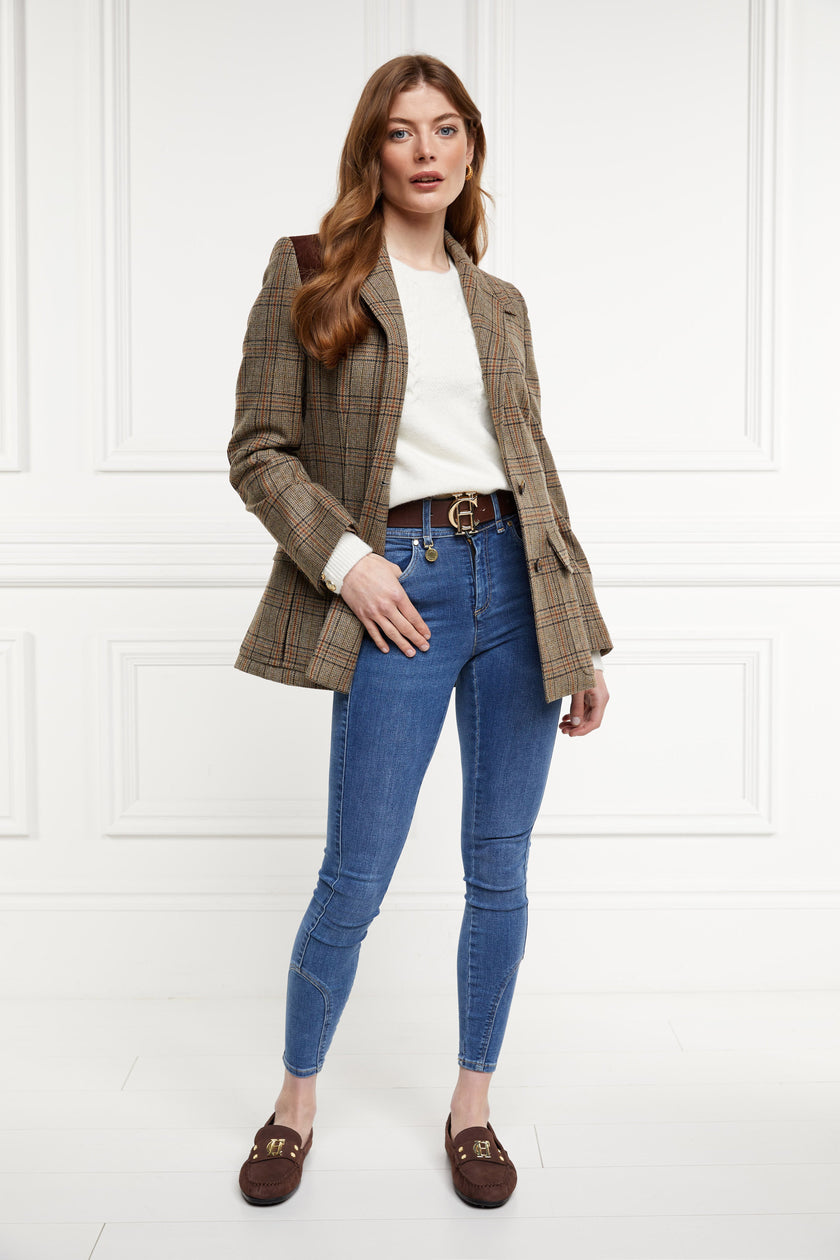 Classic brown suede loafers with a leather sole and top stitching details and gold hardware paired with skinny denim jeans, brown belt, cream crew neck knit and bredon tweed blazer