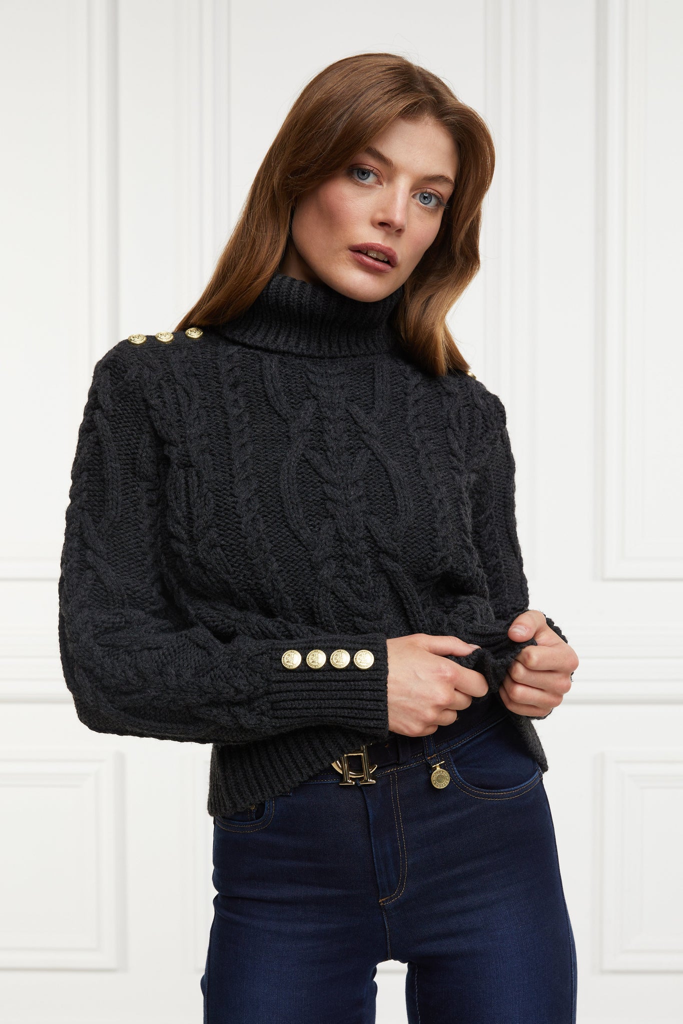 a chunky cable knit roll neck jumper in dark grey with dropped shoulders and thick ribbed cable trims and gold buttons on cuffs and collar