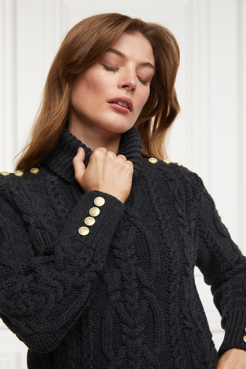 a chunky cable knit roll neck jumper in dark grey with dropped shoulders and thick ribbed cable trims and gold buttons on cuffs and collar