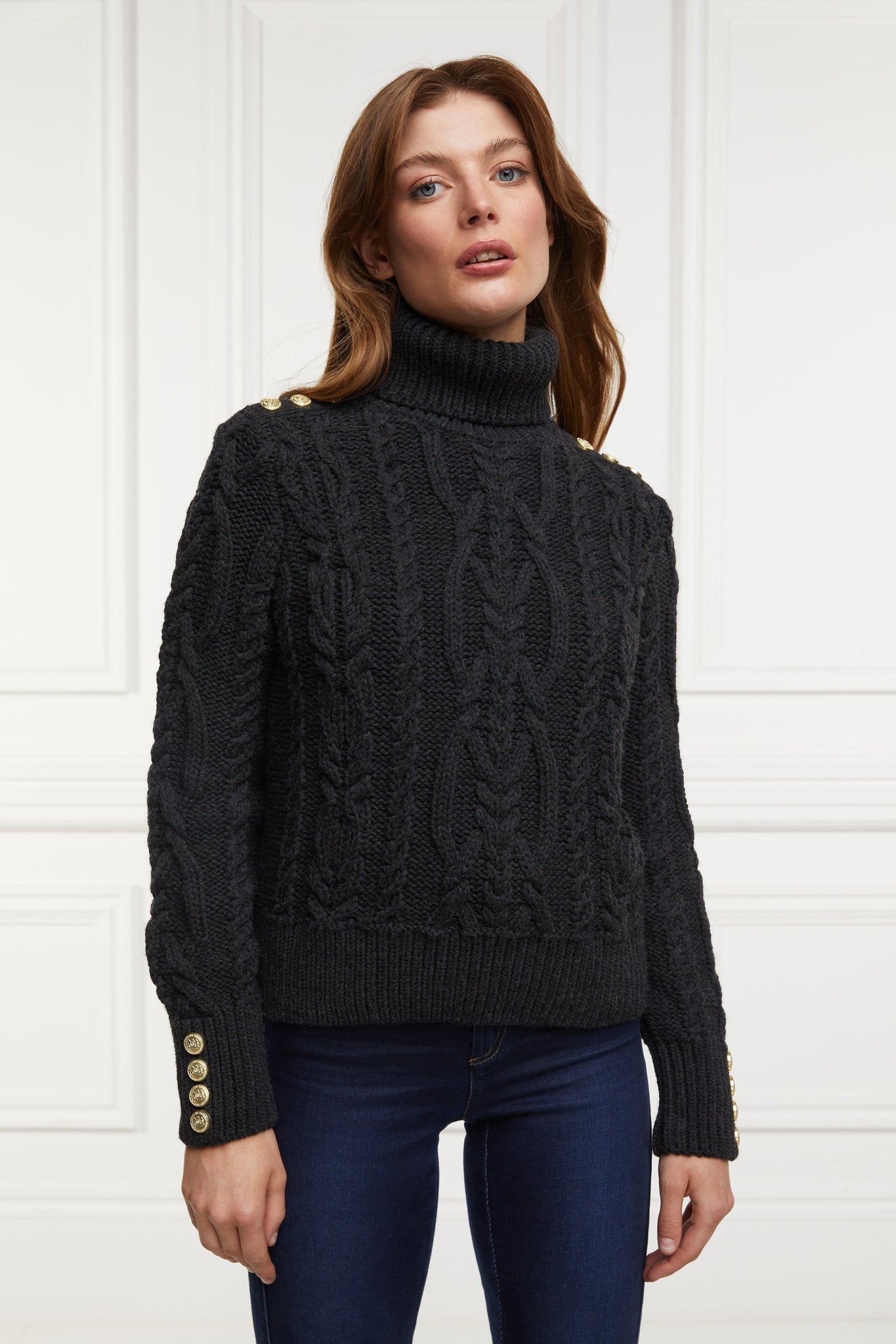 a chunky cable knit roll neck jumper in dark grey with dropped shoulders and thick ribbed cable trims and gold buttons on cuffs and collar