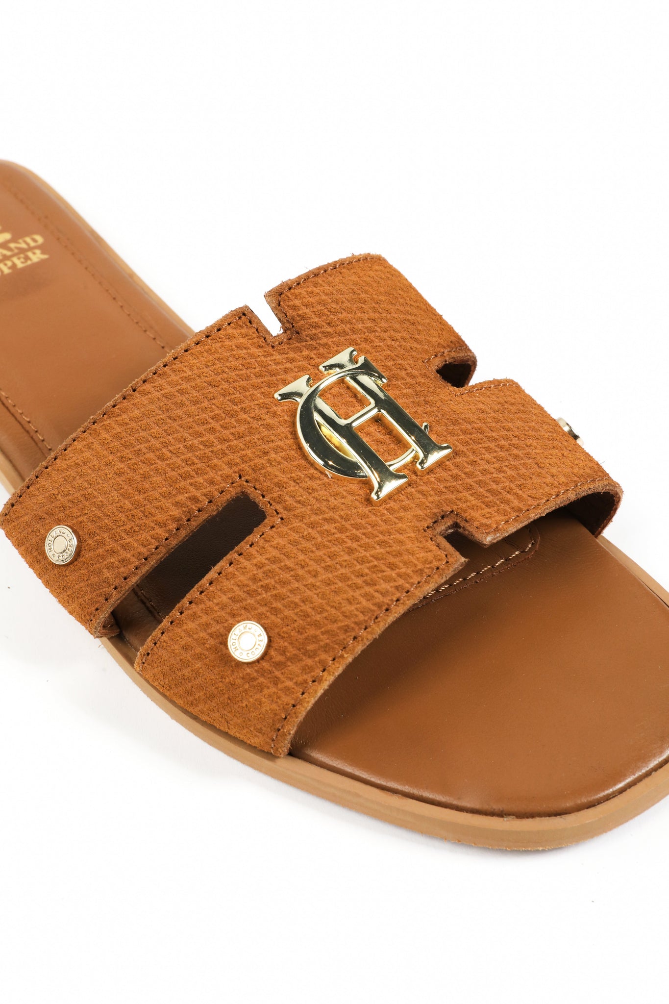 Close up of gold hardware on tan suede sliders with a tan leather sole