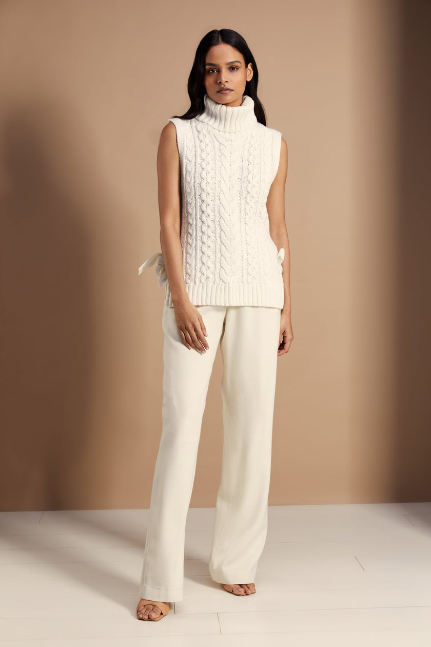 Sleeveless white chunky knit cable jumper with a roll neck and ties at each side 