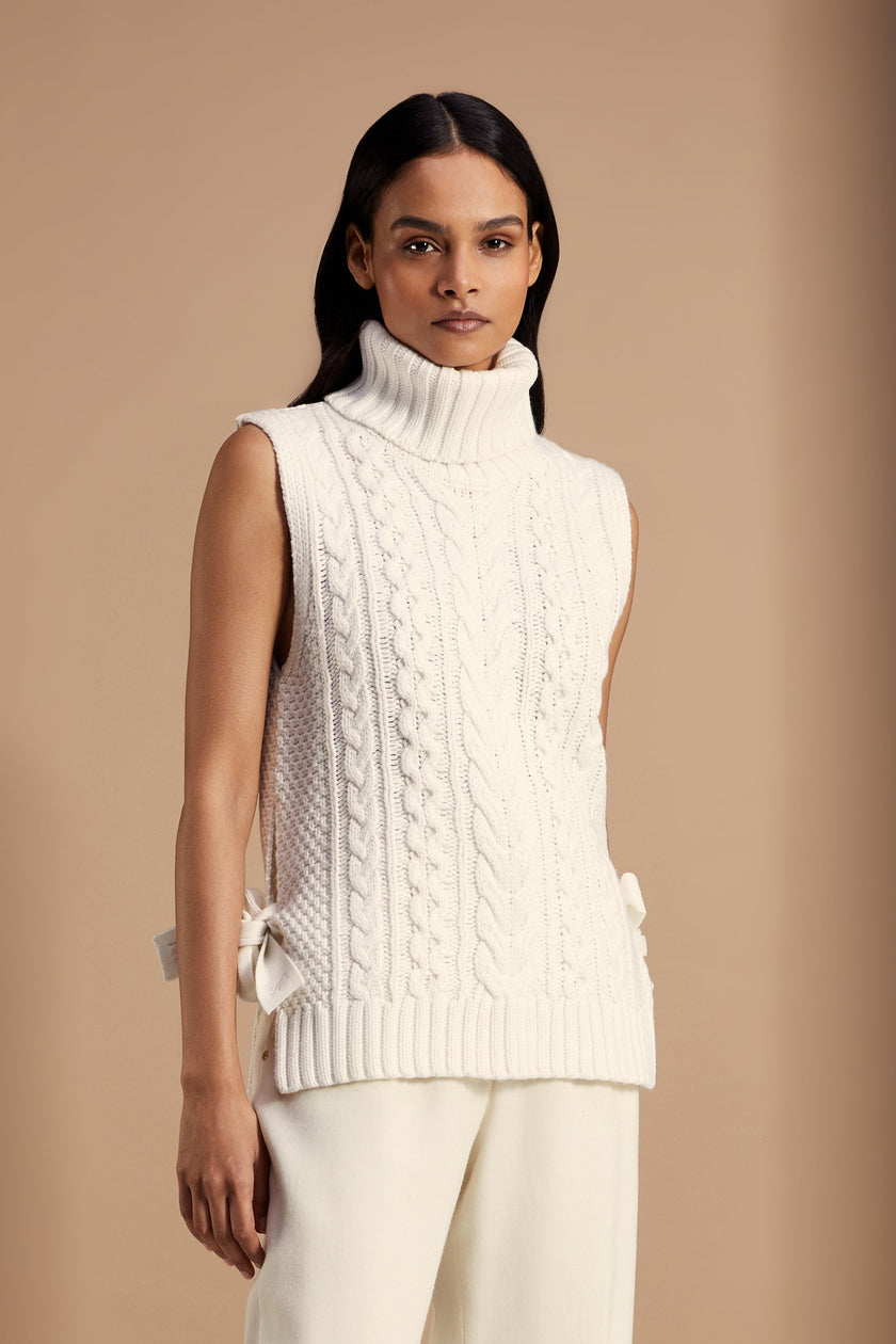 Sleeveless white chunky knit cable jumper with a roll neck and ties at each side 