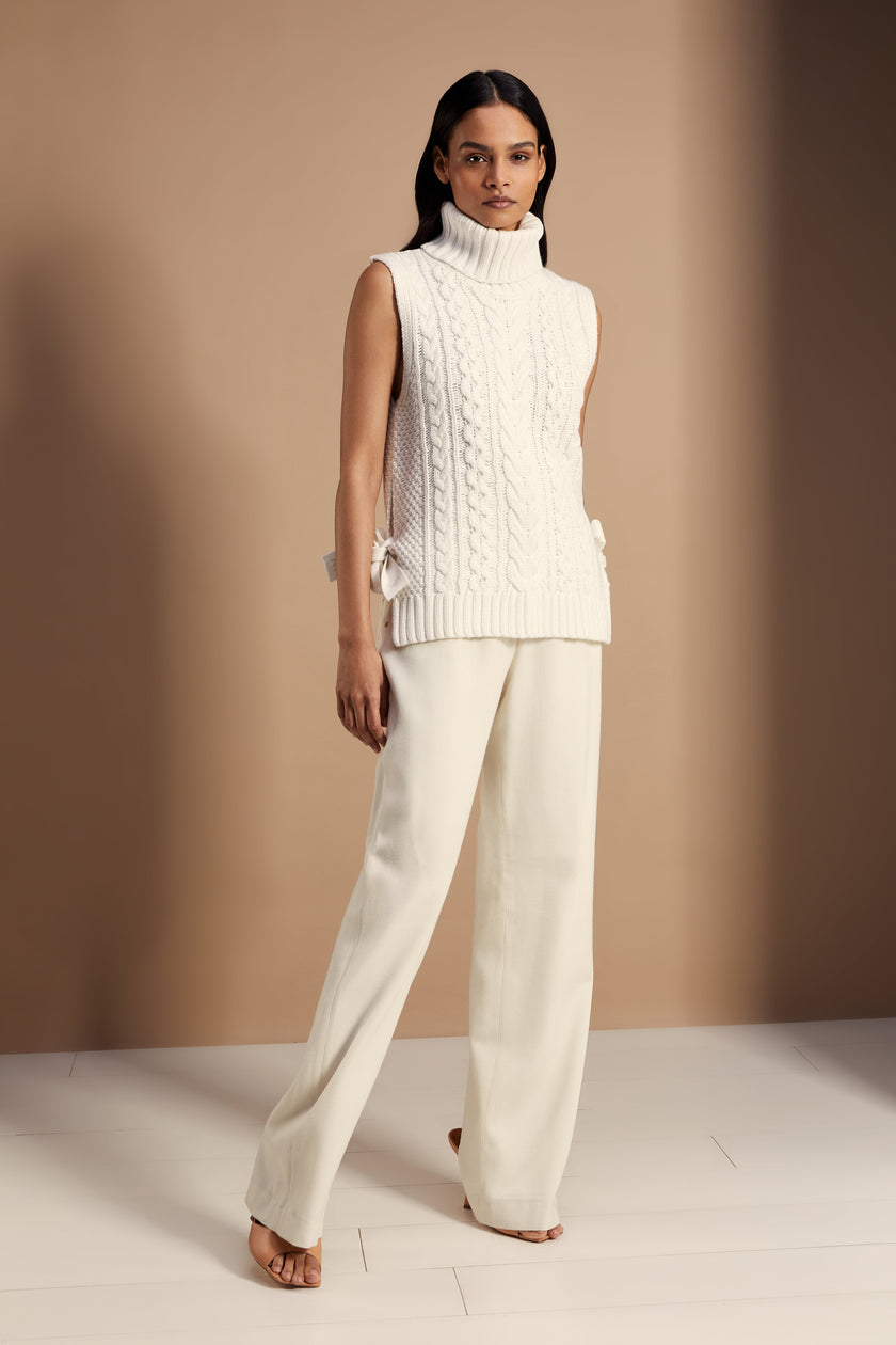 Sleeveless white chunky knit cable jumper with a roll neck and ties at each side 