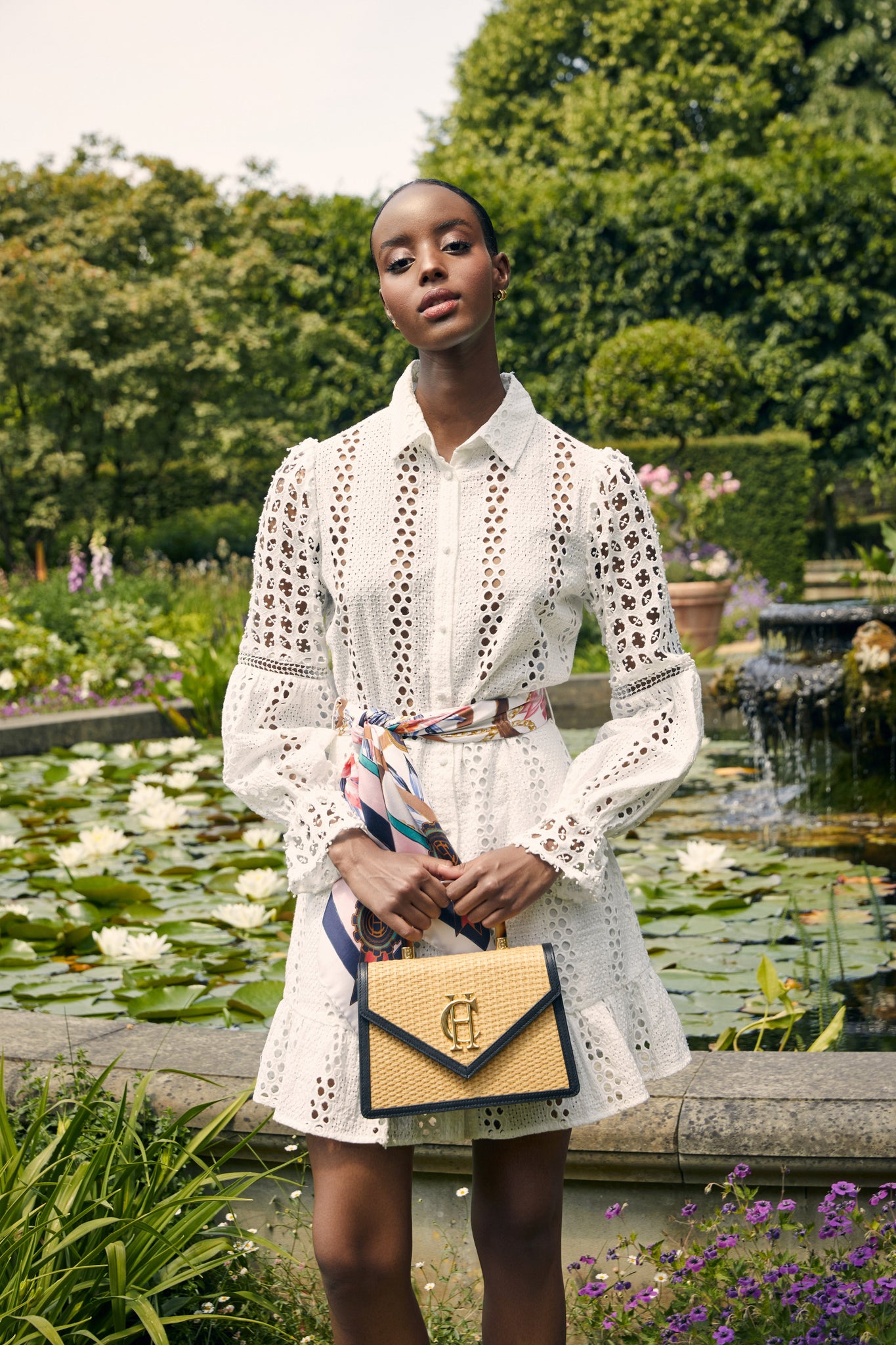 Womens white mini dress in broderie lace with a white and pink scarf around the waist and a black and natural raffia bag