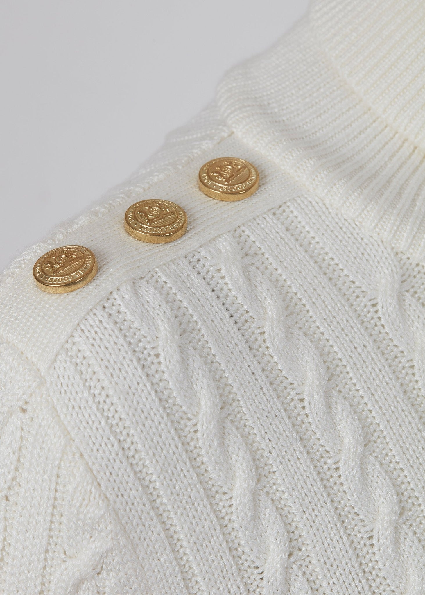 gold button detail across shoulder of womens cable knit jumper in white with ribbed roll neck cuffs and hem