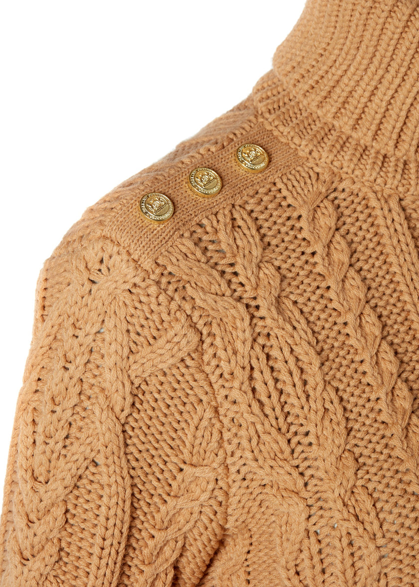 gold button detail across shoulders of a chunky cable knit roll neck jumper in camel with dropped shoulders and thick ribbed cable trims and gold buttons on cuffs and collar