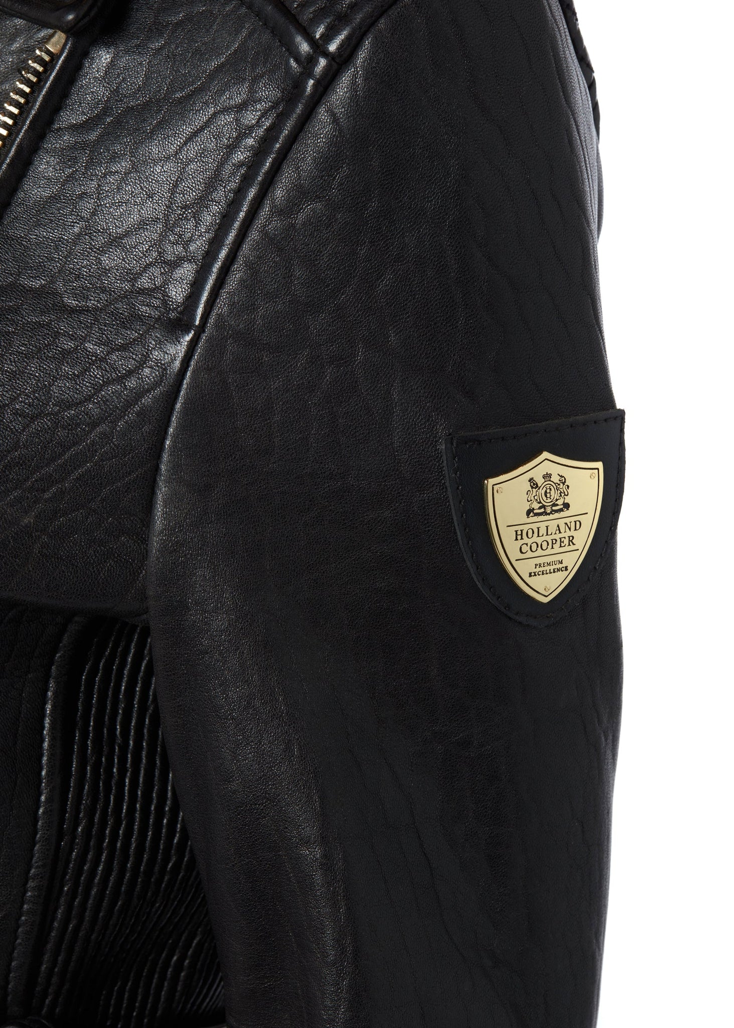 gold shield detail on arm of womens leather longline biker jacket in black with shirred side panels pin-tucking on the shoulders and a belted waist detailed with golf zips and small shield badge on arm