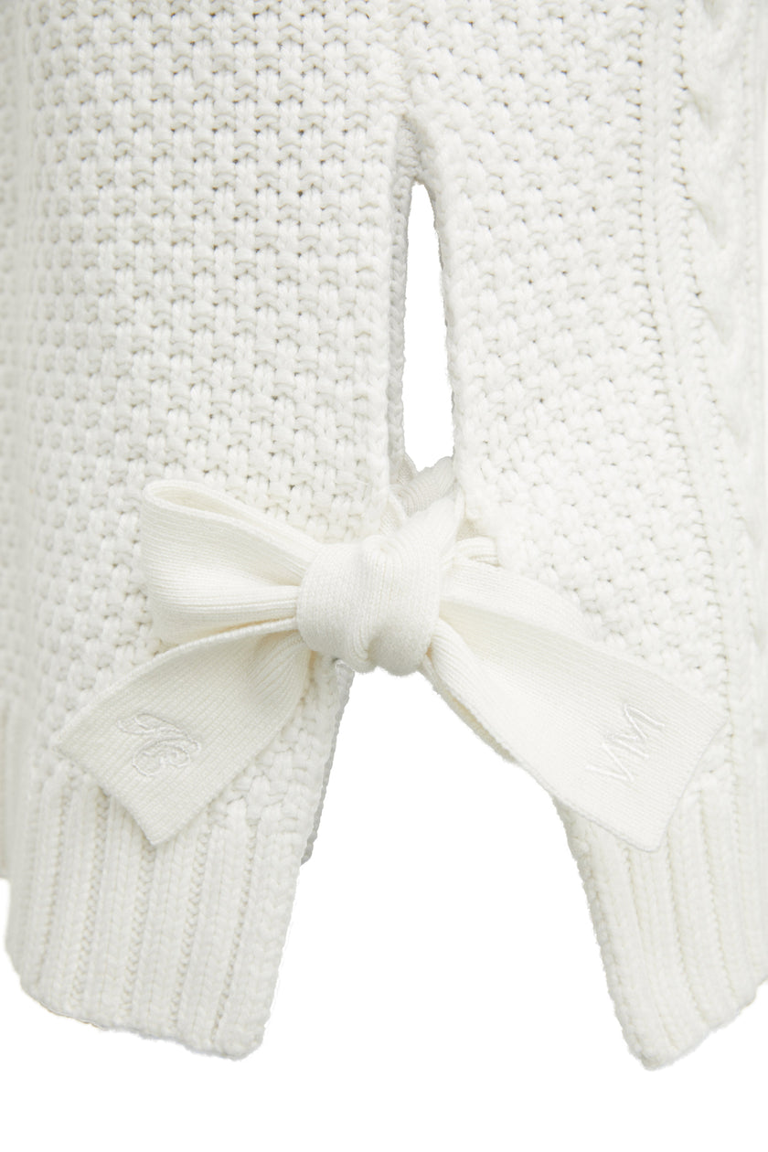 Detail of side tie and embroidered branding on Sleeveless white chunky knit cable jumper with a roll neck 