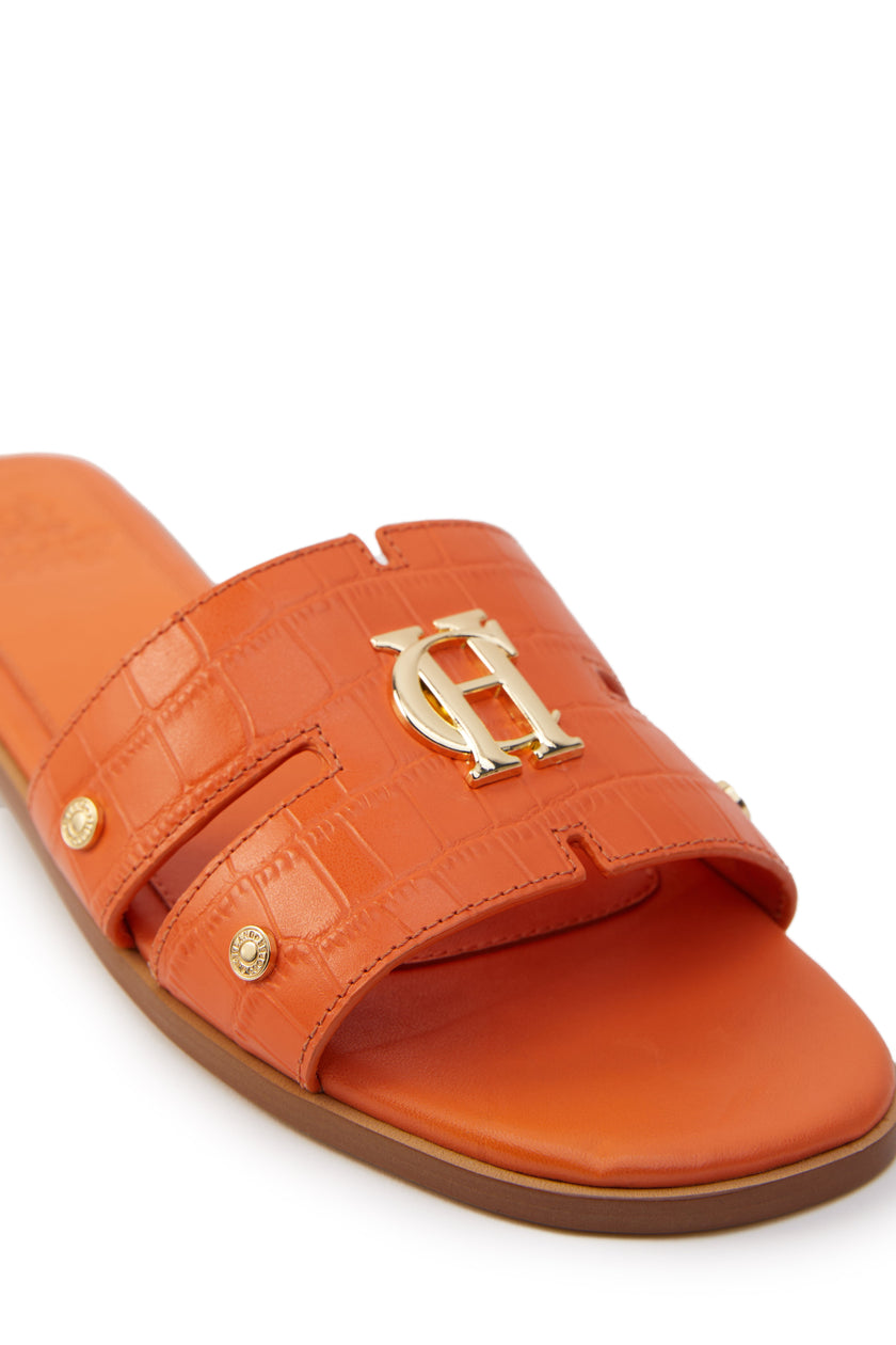 Close up of orange croc embossed leather sliders with a tan leather sole and gold hardware. 