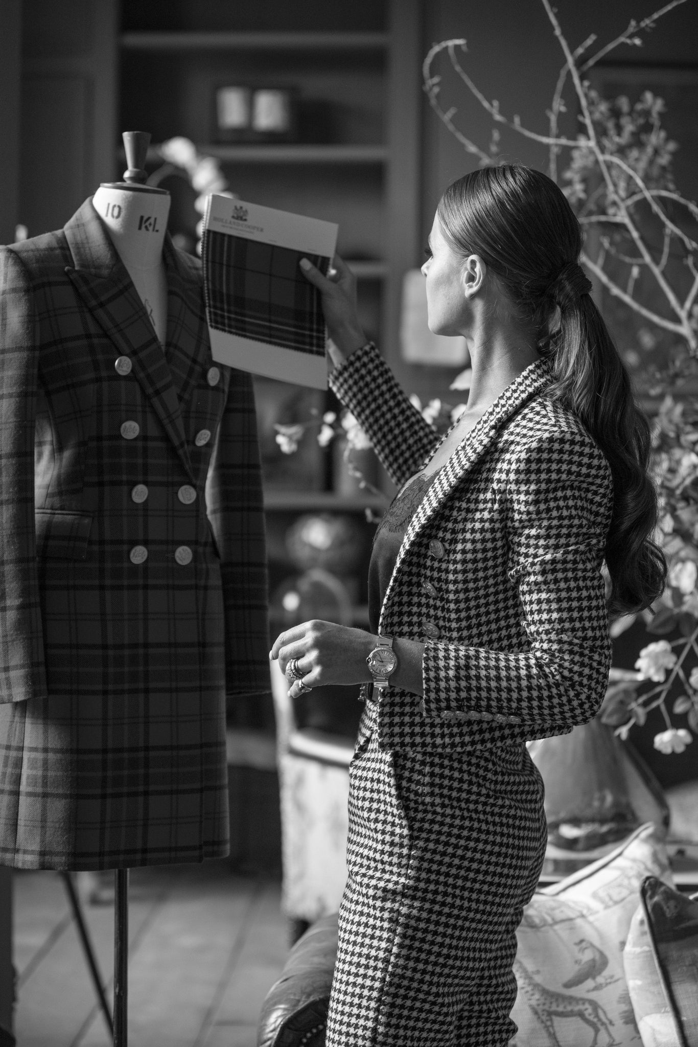 Black and White image of Jade Holland Cooper holds tartan sample against tartan womens blazer on mannequin